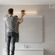 Person installing bathroom vanity light above mirror in modern bathroom setting.