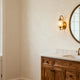 Bathroom vanity lights guide featuring stylish wall sconces illuminating a wooden vanity and round mirror.